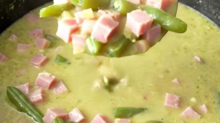 A bowl of creamy ham and potato soup with visible chunks of ham and green beans.