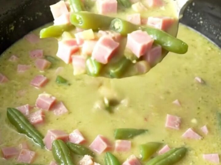 A bowl of creamy ham and potato soup with visible chunks of ham and green beans.