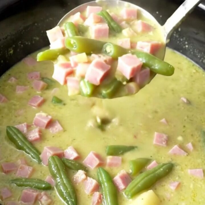 A bowl of creamy ham and potato soup with visible chunks of ham and green beans.