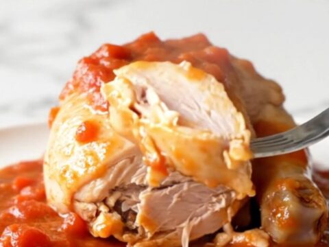 A close-up view of cooked chicken breasts covered in a thick, savory tomato gravy with soft onions and green peppers.