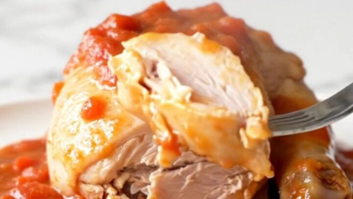 A close-up view of cooked chicken breasts covered in a thick, savory tomato gravy with soft onions and green peppers.
