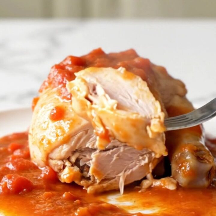 A close-up view of cooked chicken breasts covered in a thick, savory tomato gravy with soft onions and green peppers.