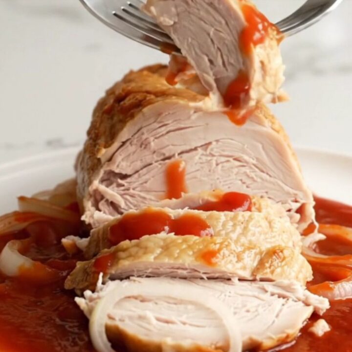 A sliced, succulent slow-cooked turkey breast covered in a rich, dark cherry cola and onion glaze on a white plate.