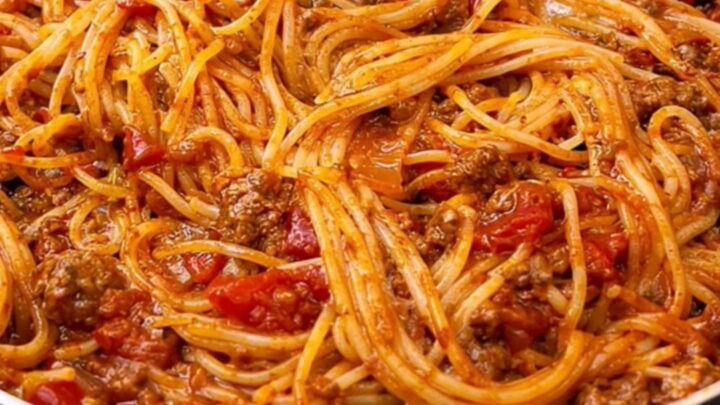 A close-up of a fork twisting glossy spaghetti coated in a rich, hearty ground beef tomato sauce.