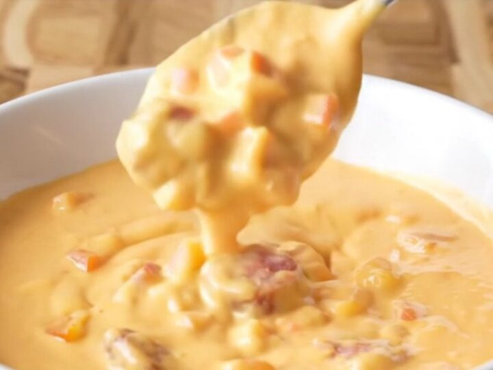 A close-up view of creamy, pale orange Cajun queso in a slow cooker