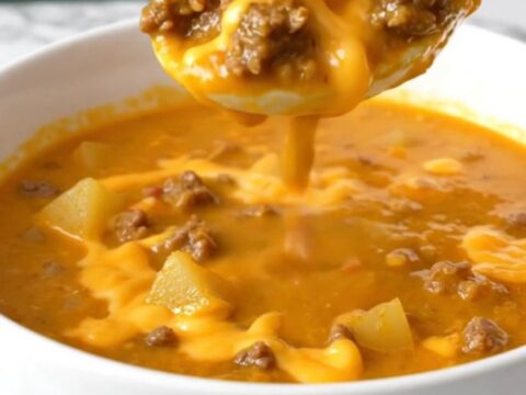 A steaming bowl of thick, orange cheeseburger soup filled with beef crumbles, potato cubes, and green chiles.