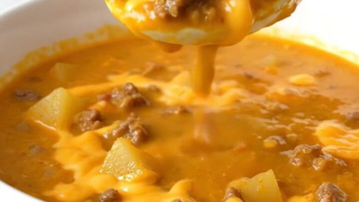 A steaming bowl of thick, orange cheeseburger soup filled with beef crumbles, potato cubes, and green chiles.