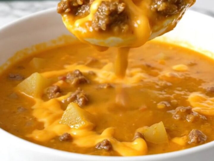 A steaming bowl of thick, orange cheeseburger soup filled with beef crumbles, potato cubes, and green chiles.
