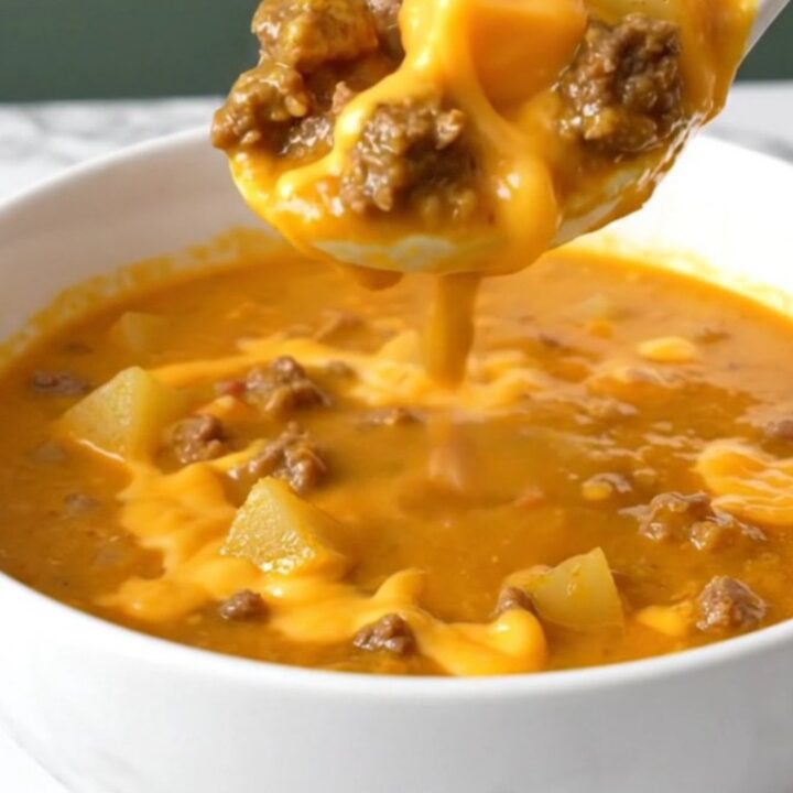 A steaming bowl of thick, orange cheeseburger soup filled with beef crumbles, potato cubes, and green chiles.