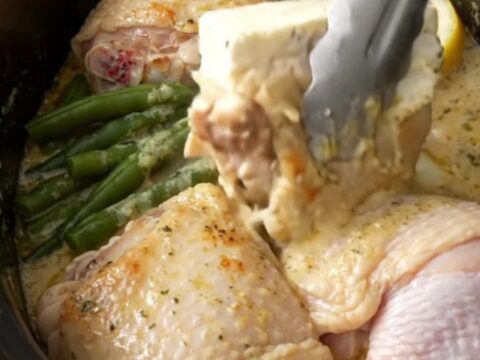 Slow cooker filled with cooked chicken thighs, green beans, and a creamy lemon herb sauce.