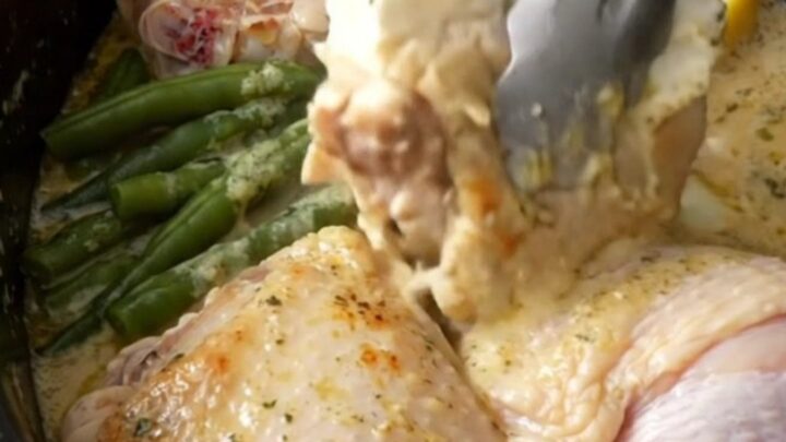 Slow cooker filled with cooked chicken thighs, green beans, and a creamy lemon herb sauce.