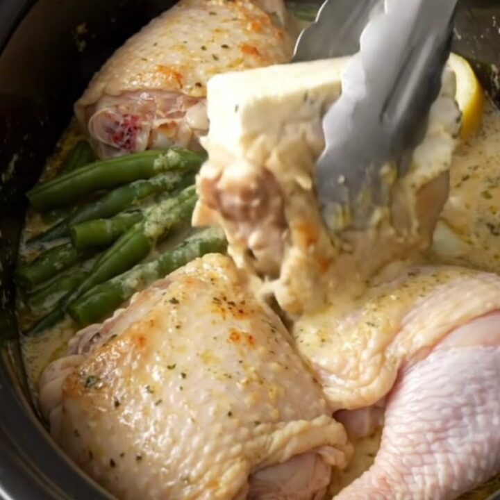 Slow cooker filled with cooked chicken thighs, green beans, and a creamy lemon herb sauce.