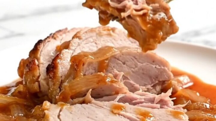 Close-up of tender, slow-cooked pork loin slices topped with caramelized onions and a glossy