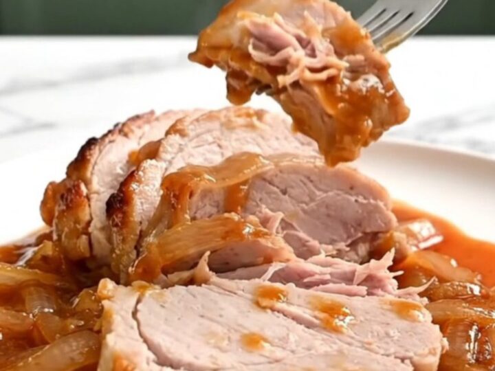 Close-up of tender, slow-cooked pork loin slices topped with caramelized onions and a glossy