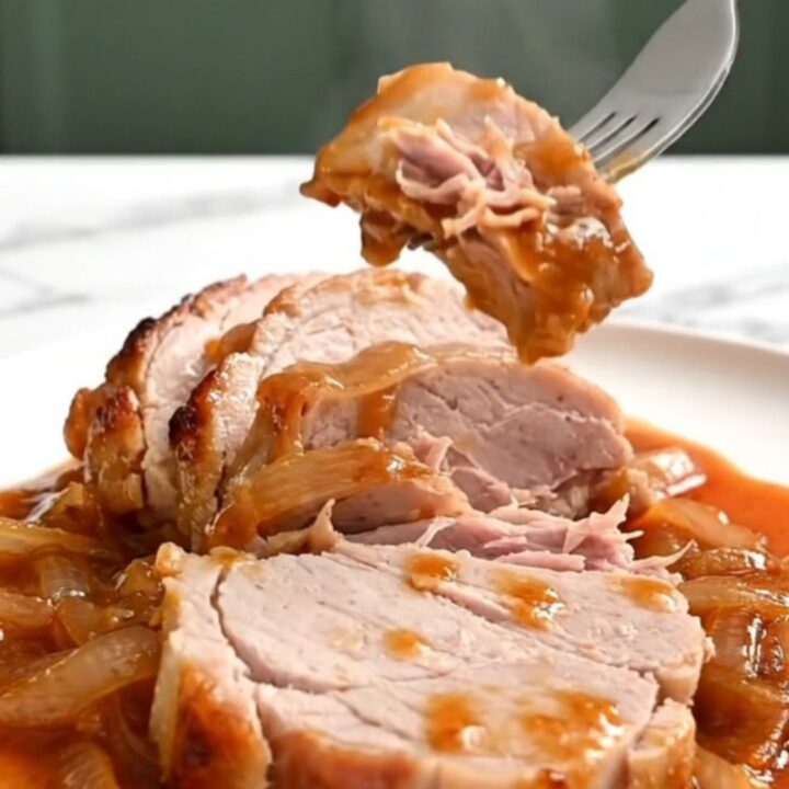 Close-up of tender, slow-cooked pork loin slices topped with caramelized onions and a glossy