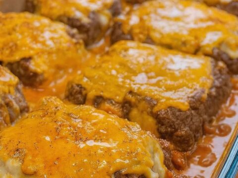 A 9x13 glass casserole dish filled with six golden, cheese-topped hamburger steaks bubbling in rich gravy.