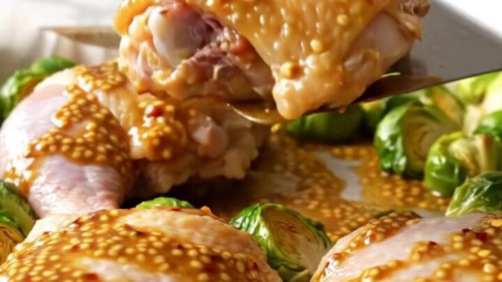 A sheet pan filled with golden-brown roasted chicken thighs and caramelized Brussels sprouts drizzled with a honey mustard