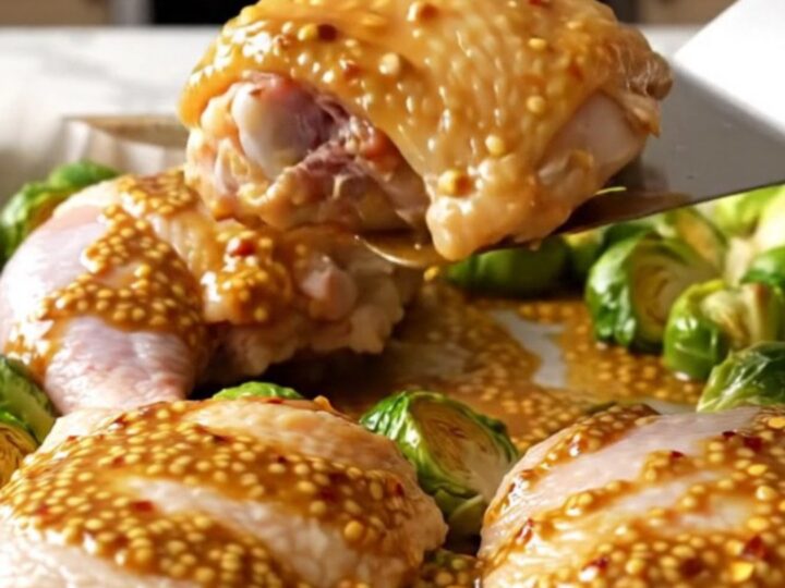 A sheet pan filled with golden-brown roasted chicken thighs and caramelized Brussels sprouts drizzled with a honey mustard