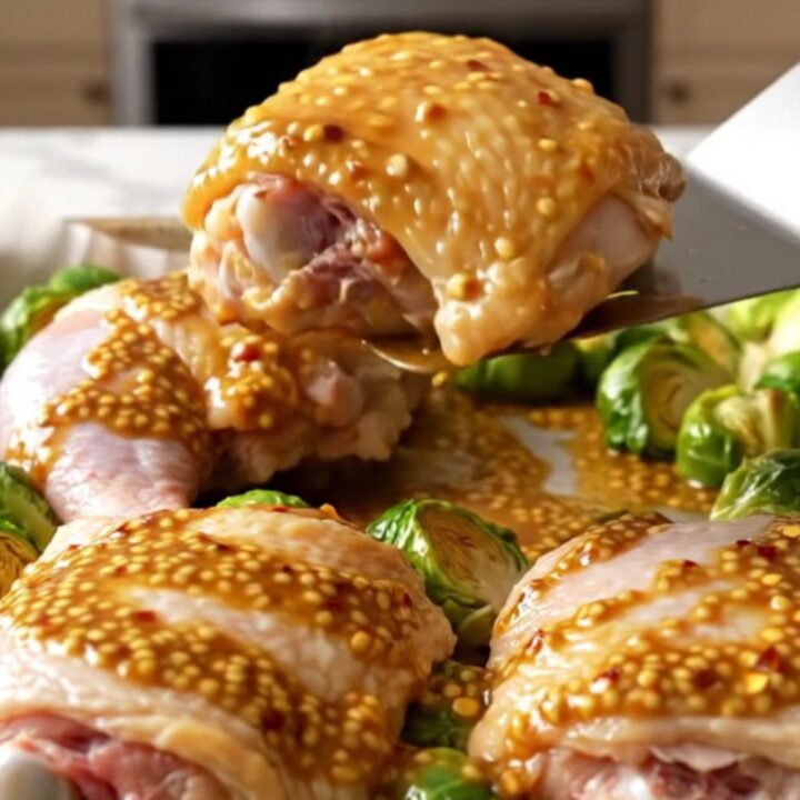 A sheet pan filled with golden-brown roasted chicken thighs and caramelized Brussels sprouts drizzled with a honey mustard