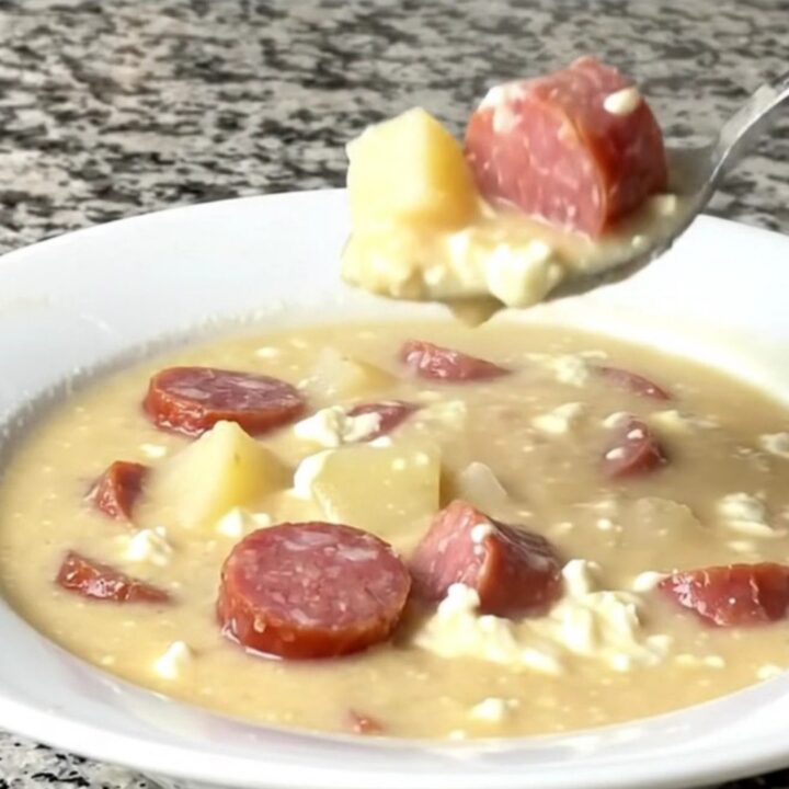 A close-up view of the creamy kielbasa potato soup in a black slow cooker insert, showing chunks of potato and sausage.