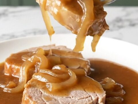 A close-up view of cooked pork steaks smothered in a rich brown onion gravy on a white plate.