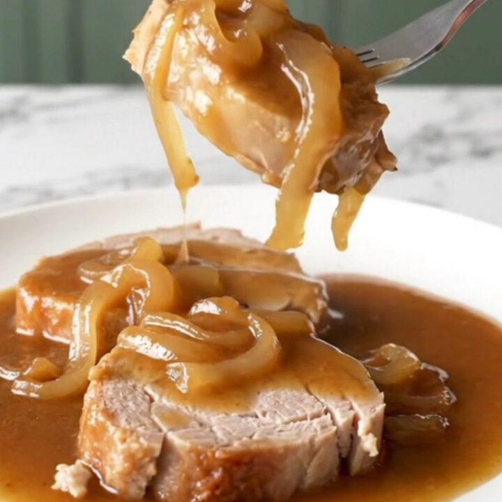 A close-up view of cooked pork steaks smothered in a rich brown onion gravy on a white plate.