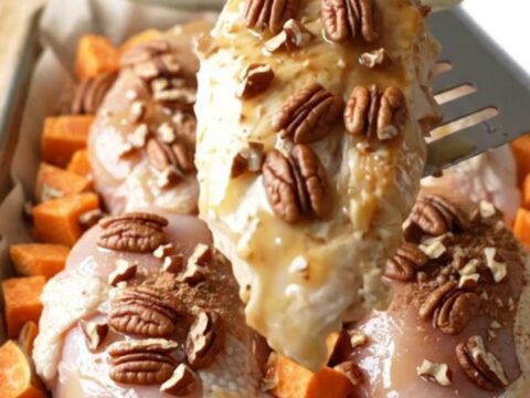 A sheet pan filled with golden-brown chicken breasts and roasted sweet potato cubes topped with toasted pecans.