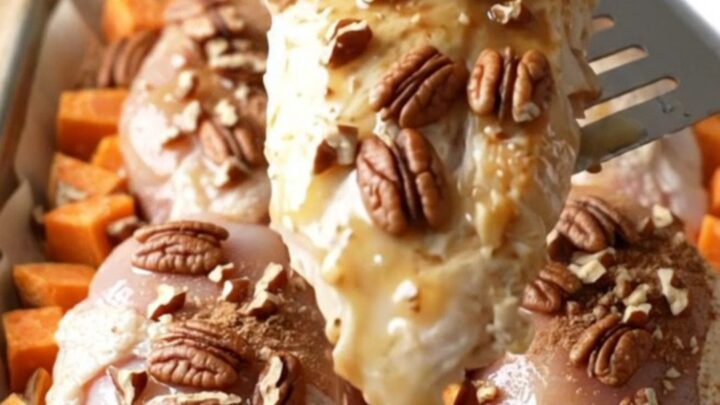 A sheet pan filled with golden-brown chicken breasts and roasted sweet potato cubes topped with toasted pecans.