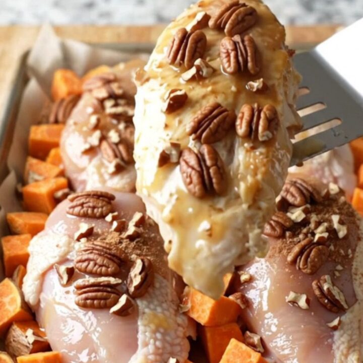 A sheet pan filled with golden-brown chicken breasts and roasted sweet potato cubes topped with toasted pecans.