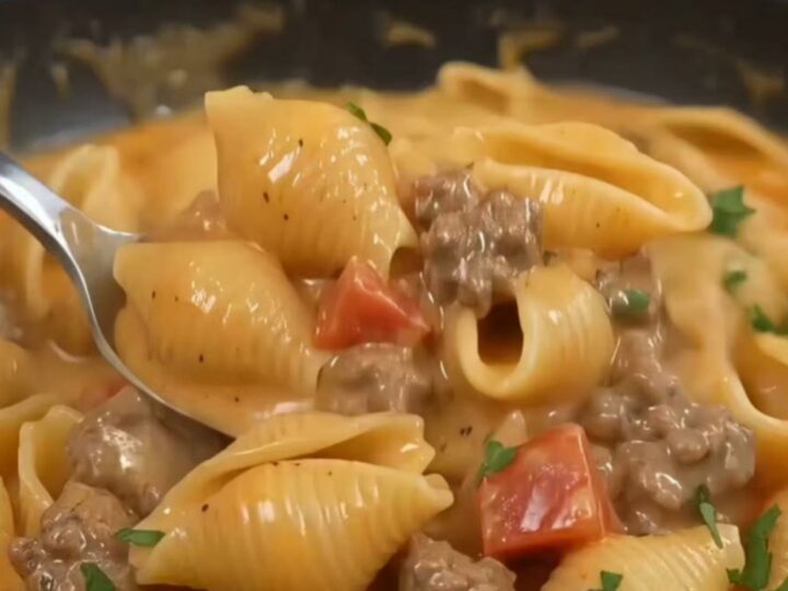 A close-up of creamy pasta shells with minced beef and mushrooms in a black skillet.