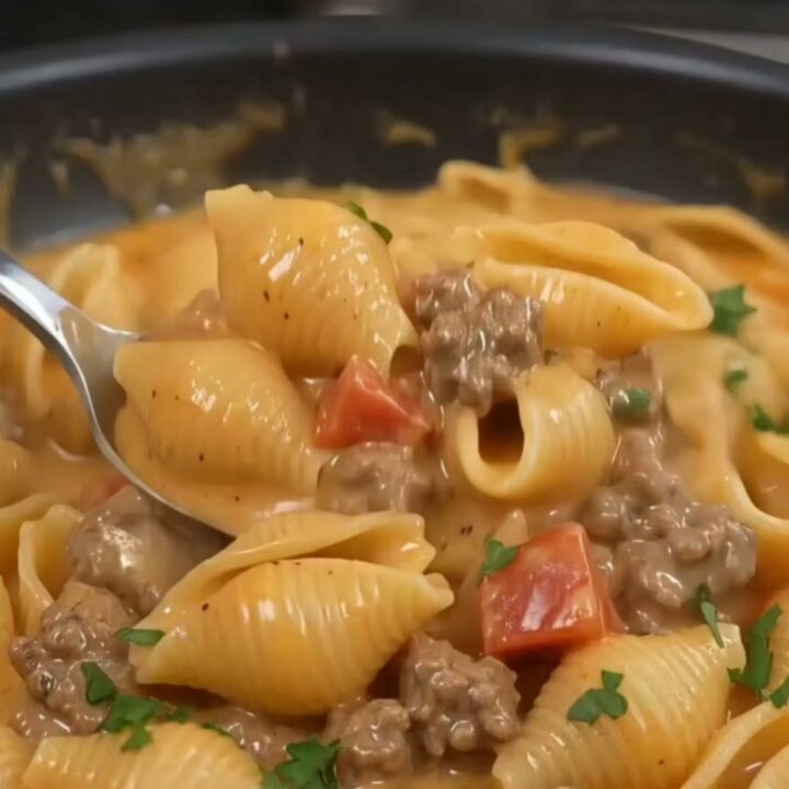 A close-up of creamy pasta shells with minced beef and mushrooms in a black skillet.