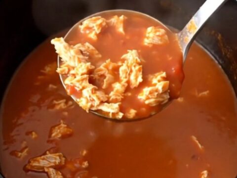 A close-up of a steaming bowl of tomato-based turkey and banana pepper soup in a dark stoneware bowl.
