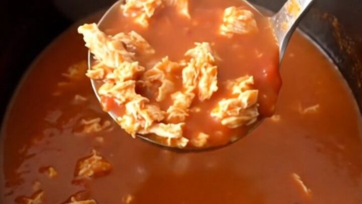 A close-up of a steaming bowl of tomato-based turkey and banana pepper soup in a dark stoneware bowl.