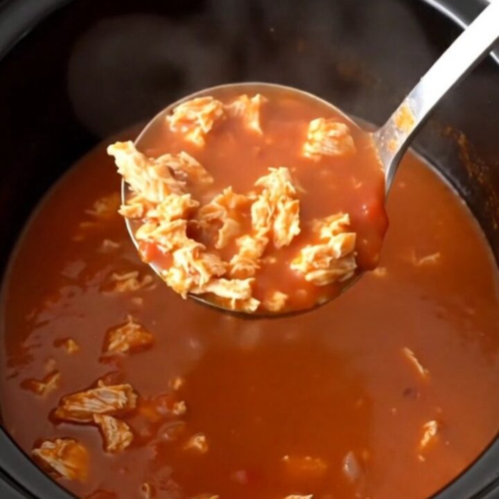 A close-up of a steaming bowl of tomato-based turkey and banana pepper soup in a dark stoneware bowl.