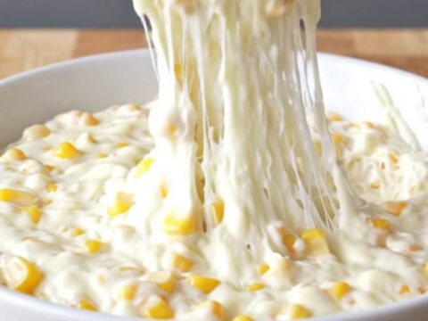 A top-down view of a slow cooker filled with golden corn kernels, shredded mozzarella, and creamy seasonings.