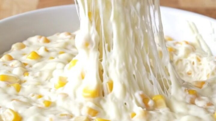 A top-down view of a slow cooker filled with golden corn kernels, shredded mozzarella, and creamy seasonings.