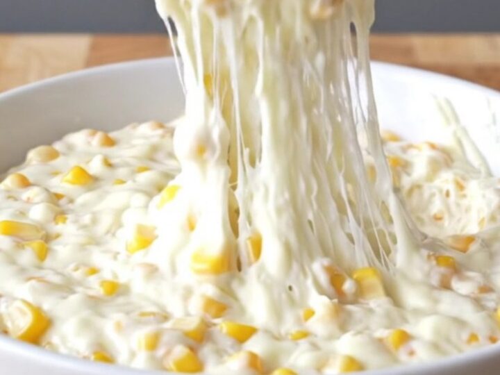 A top-down view of a slow cooker filled with golden corn kernels, shredded mozzarella, and creamy seasonings.
