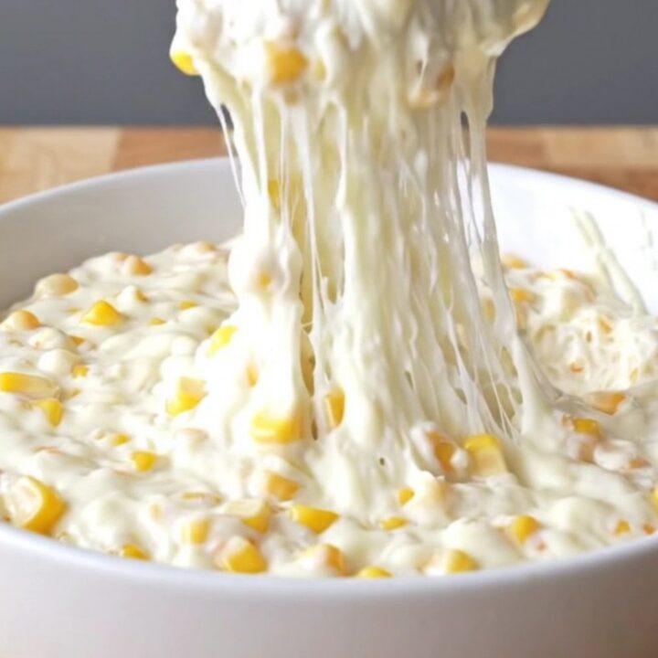 A top-down view of a slow cooker filled with golden corn kernels, shredded mozzarella, and creamy seasonings.