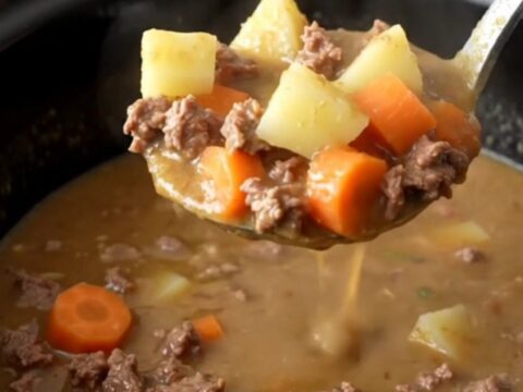 A steaming bowl of creamy slow cooker hamburger vegetable soup with visible ground beef and colorful vegetables.