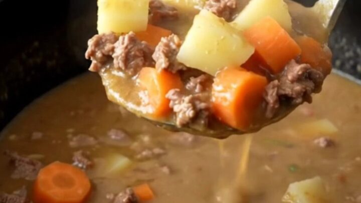A steaming bowl of creamy slow cooker hamburger vegetable soup with visible ground beef and colorful vegetables.