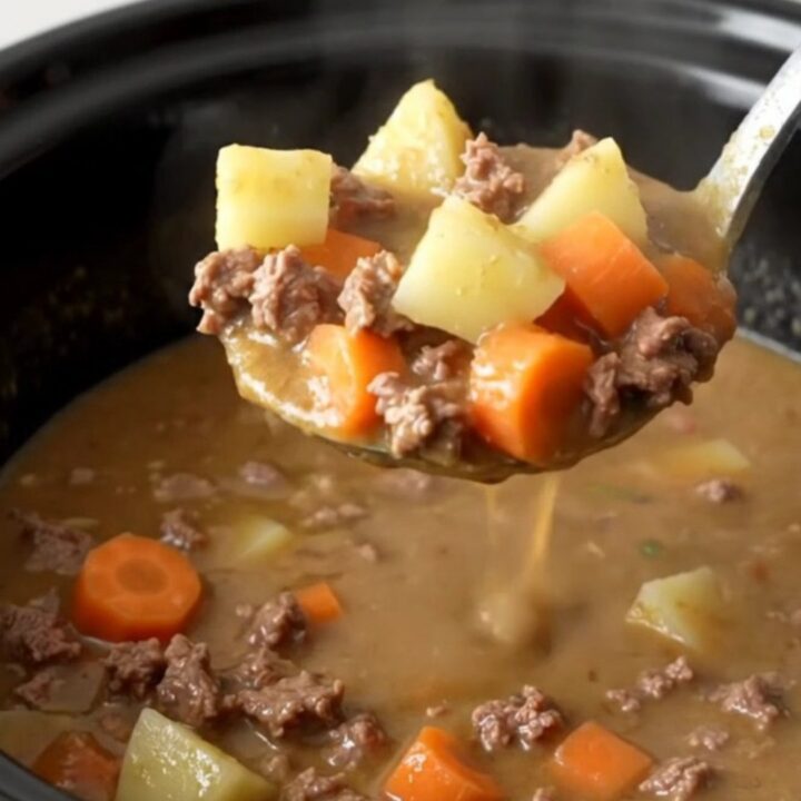 A steaming bowl of creamy slow cooker hamburger vegetable soup with visible ground beef and colorful vegetables.