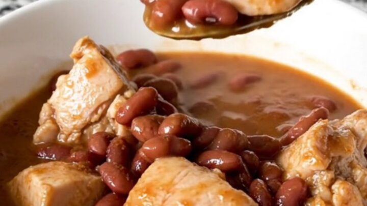 A slow cooker filled with chicken, red beans, and andouille sausage in a rich, seasoned broth.