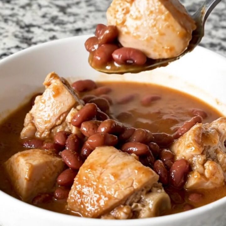 A slow cooker filled with chicken, red beans, and andouille sausage in a rich, seasoned broth.