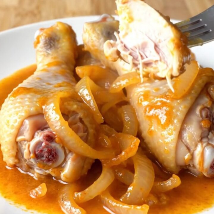 A close-up view of orange soda glazed chicken drumsticks on a white plate, showing a thick, shiny