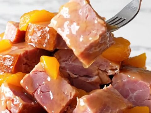 A close-up shot of slow-cooked ham chunks coated in a glossy peach and jalapeño glaze on a white marble surface.