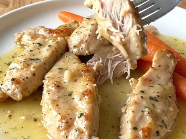 Slow cooker filled with cooked chicken tenders, baby carrots, and a creamy garlic parmesan sauce.