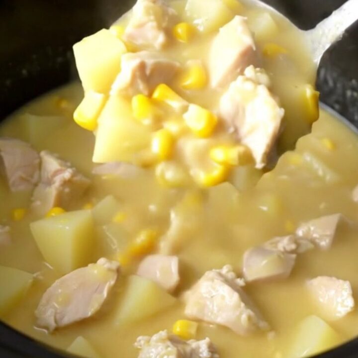A creamy, white chowder in a slow cooker filled with chicken chunks, corn, and potatoes.