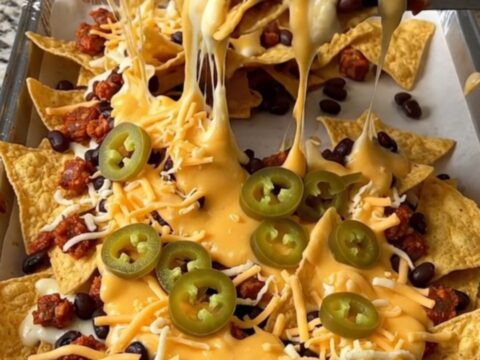 A sheet pan filled with golden tortilla chips topped with cooked chorizo, black beans, melted cheese, and jalapeno slices.