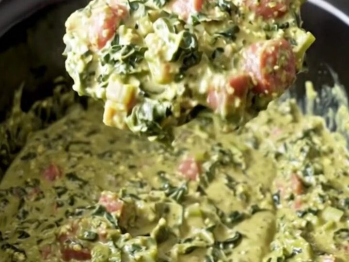A close-up view of the creamy Southern swamp dip in a black slow cooker insert, showing bits of sausage and greens.