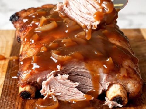 A close-up of tender, saucy country-style pork ribs in a slow cooker with visible onion slices.